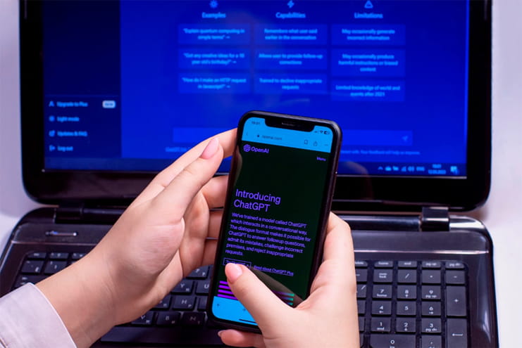 Person holding smartphone displaying ChatGPT with laptop screen in background representing AI-powered digital marketing